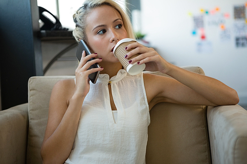 Young businesswoman having coffee while talking on phone at office