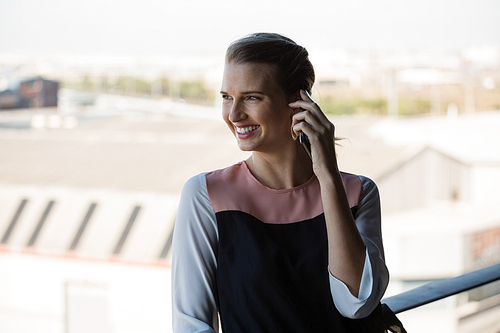 Happy young businesswoman talking on mobile phone in balcony at office
