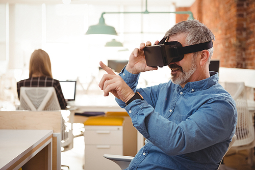 Male executive using virtual reality headset at desk in office