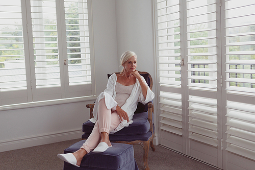 Front view of active senior Caucasian woman with hand on chin sitting on chair in a comfortable home
