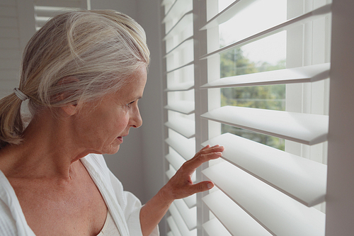 Side view of active senior Caucasian woman looking through window in a comfortable home