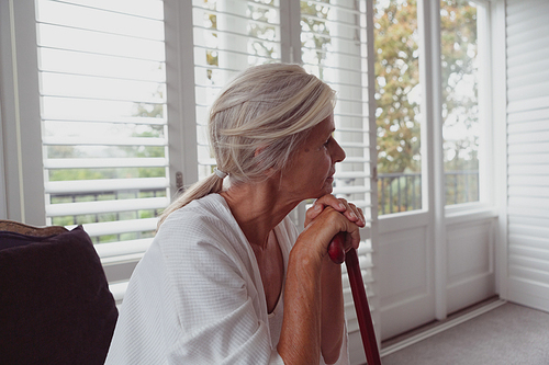 Side view of active senior Caucasian woman leaning on walking cane and looking away in a comfortable home