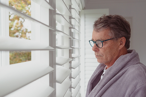 Side view of active senior Caucasian man looking through window in a comfortable home
