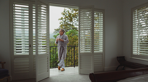 Front view of thoughtful active senior Caucasian man with coffee cup standing in balcony in a comfortable home