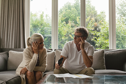 Front view of active senior Caucasian couple calculating domestic bills on sofa in living room at comfortable home