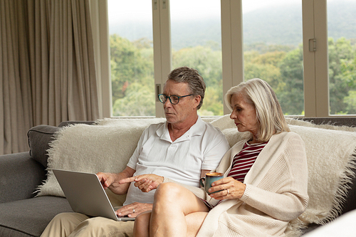 Side view of active senior Caucasian couple discussing over laptop on sofa in a comfortable home