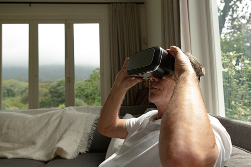 Side view of active senior Caucasian man using virtual reality headset on sofa in a comfortable home