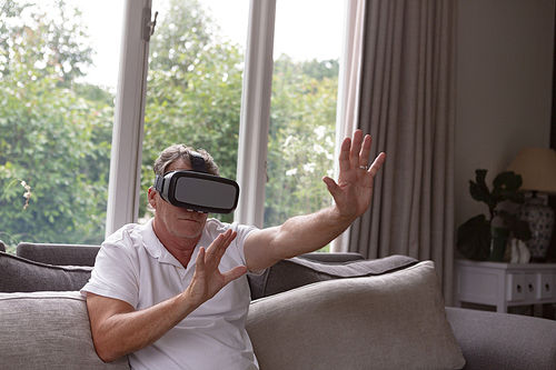 Front view of active senior Caucasian man using virtual reality headset on sofa in a comfortable home