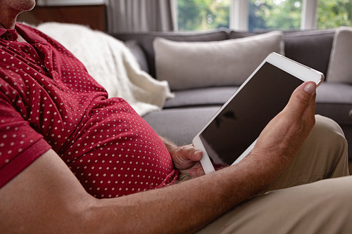 Mid section of active senior Caucasian man using digital tablet on sofa in a comfortable home