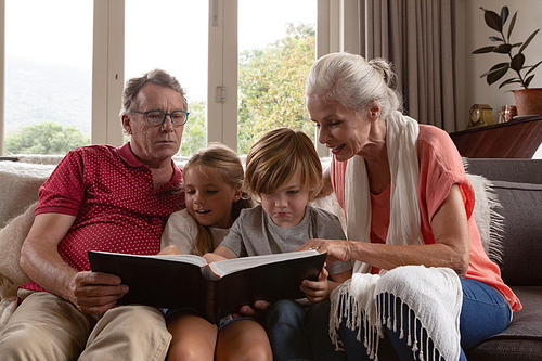 Front view of multi-generation Caucasian family looking at photo album on sofa in a comfortable home