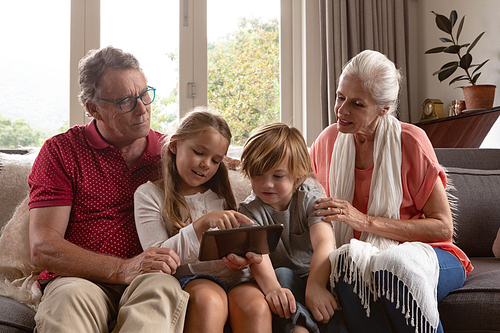 Front view of multi-generation Caucasian family using digital tablet on sofa in a comfortable home
