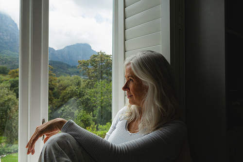Side view of thoughtful active senior Caucasian woman looking through window at home