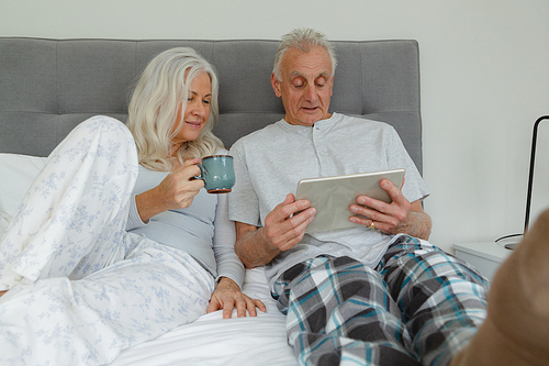 Front view of active senior Caucasian couple using digital tablet in bedroom at home