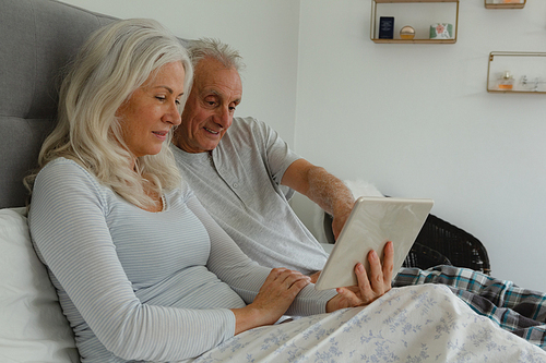 Side view of active senior Caucasian couple using digital tablet in bedroom at home