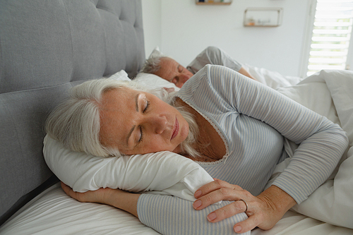 Front view of active senior Caucasian couple sleeping together in bed in bedroom at home