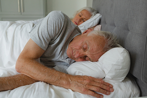 Front view of active senior Caucasian couple sleeping together in bed in bedroom