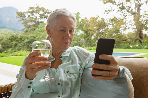 Front view of active senior Caucasian woman using mobile phone having champagne in the porch at home