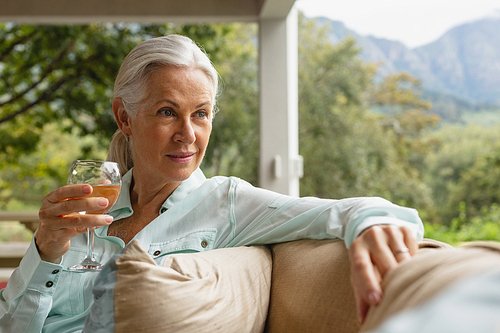 Front view of thoughtful active senior Caucasian woman having champagne in the porch at home