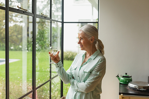 Side view of thoughtful active senior Caucasian woman having champagne at home