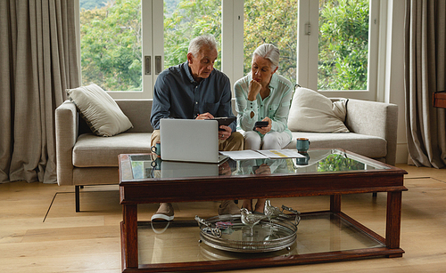 Front view of active senior Caucasian couple calculating bills in living room at home
