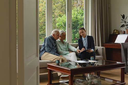 Side view of active senior Caucasian couple discussing with real estate agent over documents in living room at home