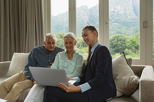 Front view of active senior Caucasian couple discussing with real estate agent over laptop in living room at home
