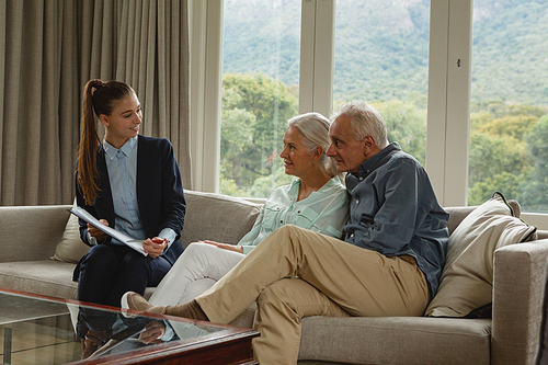 Side view of active senior Caucasian couple discussing with real estate agent over documents in living room at home