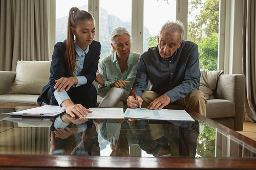 Front view of active senior Caucasian couple signing an agreement with real estate agent over documents in living room at home