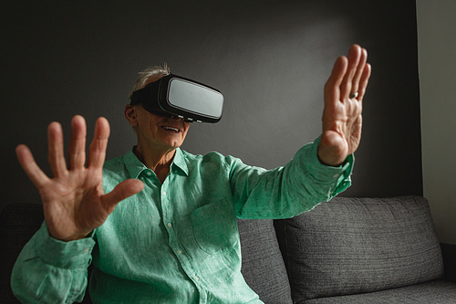 Front view of active senior Caucasian man using virtual reality headset in living room at home