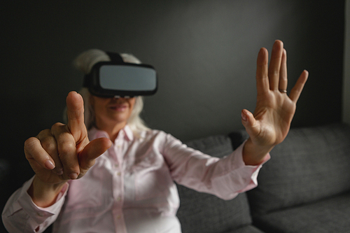 Front view of active senior Caucasian woman using virtual reality headset in living room at home