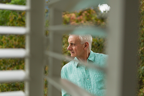 Side view of thoughtful active senior Caucasian man standing on the balcony at home
