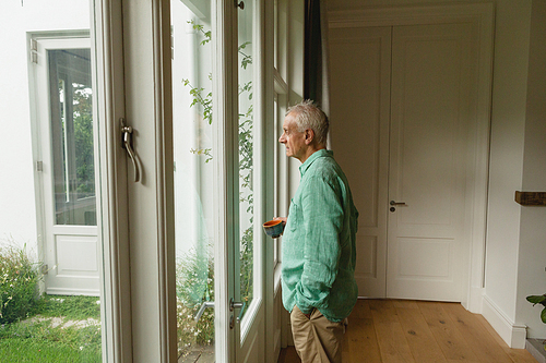 Side view of thoughtful active senior Caucasian man standing with coffee cup at home