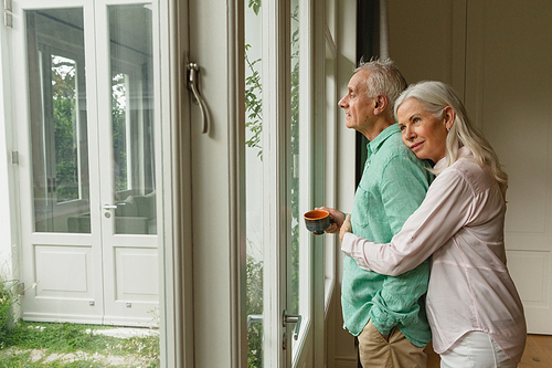 Side view of active senior Caucasian woman embracing senior man near door at home