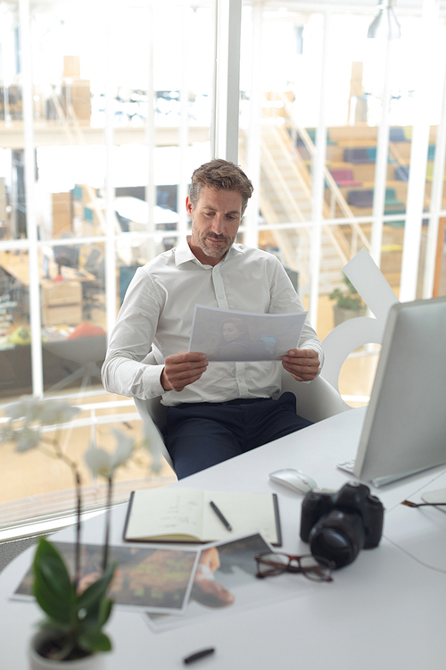 Front view of Caucasian male graphic designer looking at photograph on desk in a modern office