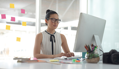 Front view of Asian female graphic designer working on computer at desk in a modern office