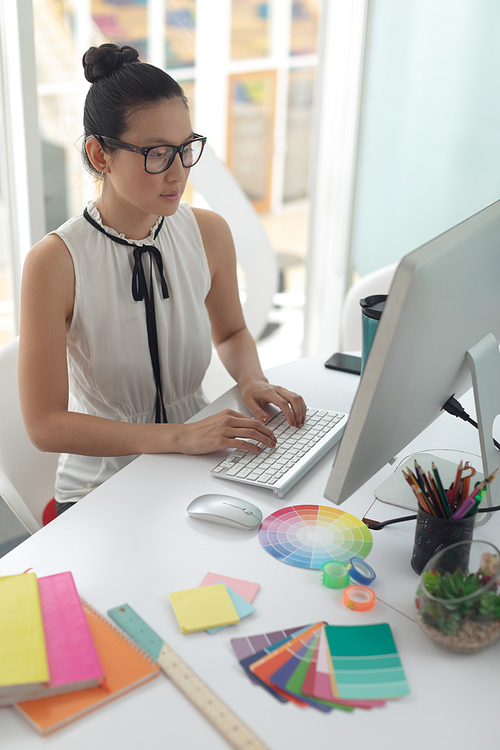 High angle view of Asian female graphic designer working on computer at desk in a modern office