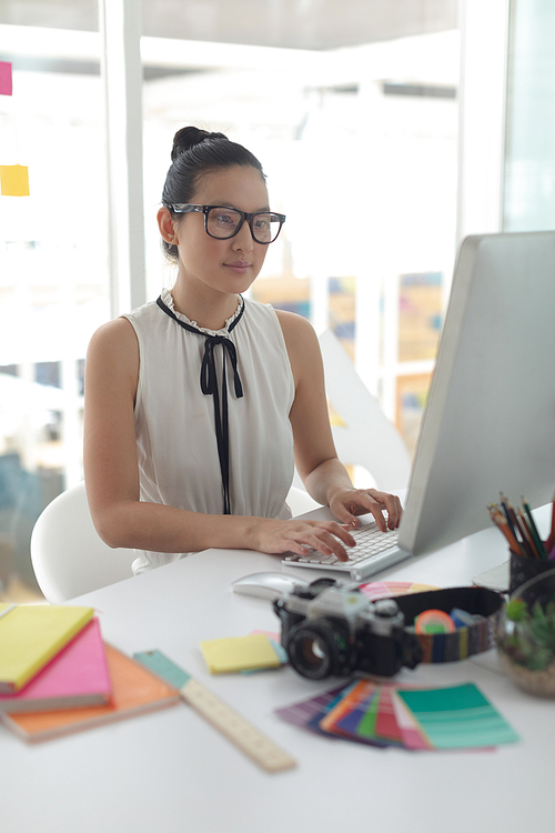 Front view of Asian female graphic designer working on computer at desk in a modern office