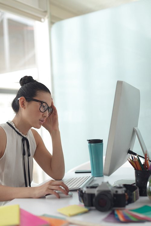 Side view of tensed Asian female graphic designer working on computer at desk in a modern office