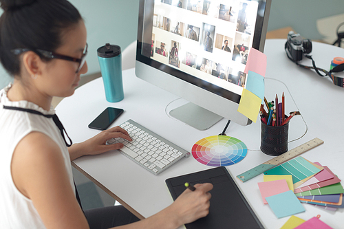 High angle view of Asian female graphic designer using graphic tablet at desk in a modern office