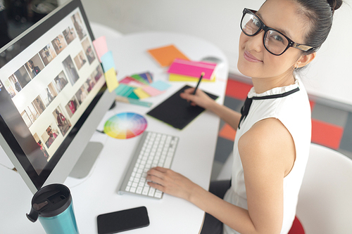 High angle view of Asian female graphic designer using graphic tablet at desk in a modern office