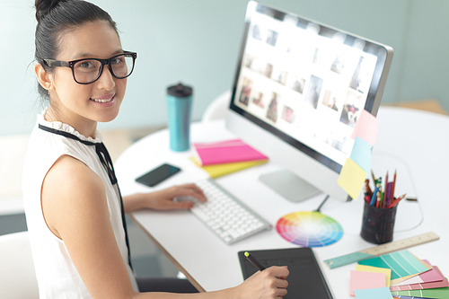 High angle view of Asian female graphic designer using graphic tablet at desk in a modern office