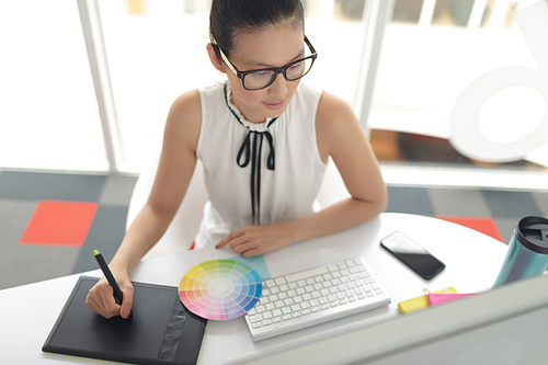 High angle view of Asian female graphic designer using graphic tablet at desk in a modern office