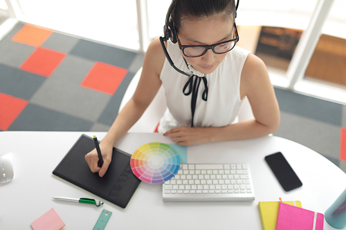 High angle view of female graphic designer using graphic tablet at desk in a modern office