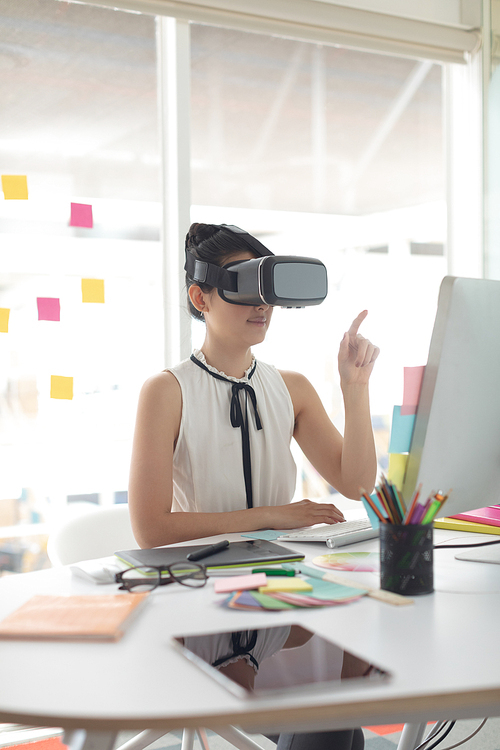 Side view of beautiful Asian female graphic designer using virtual reality headset at desk in a modern office