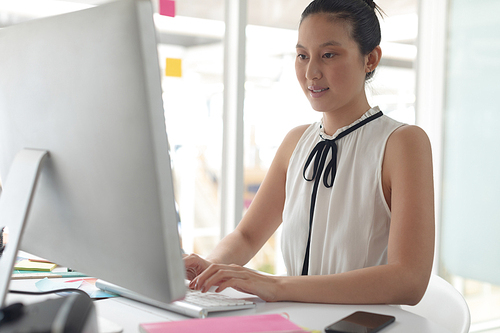 Front view of Asian female graphic designer working on computer at desk in a modern office