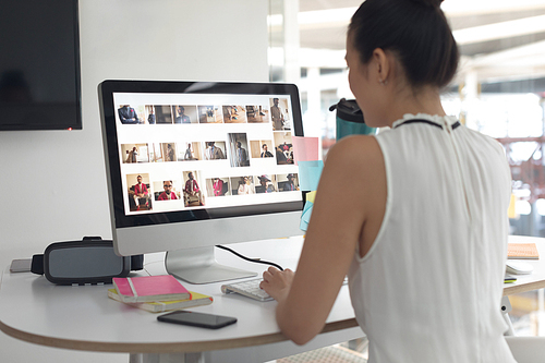 Rear view of Asian female graphic designer drinking water while working on computer at desk in a modern office