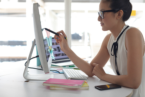 Side view of Asian female graphic designer working on computer at desk in a modern office