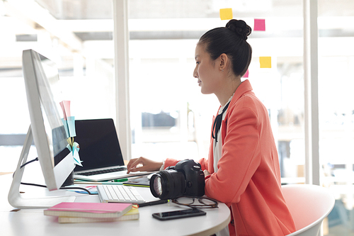 Side view of Asian female graphic designer working on laptop at desk in a modern office