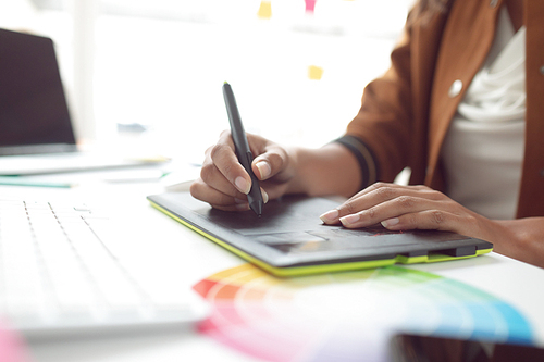 Mid section of Asian female graphic designer using graphic tablet at desk in a modern office