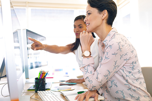 Side view of diverse female graphic designers discussing on computer at desk in a modern office